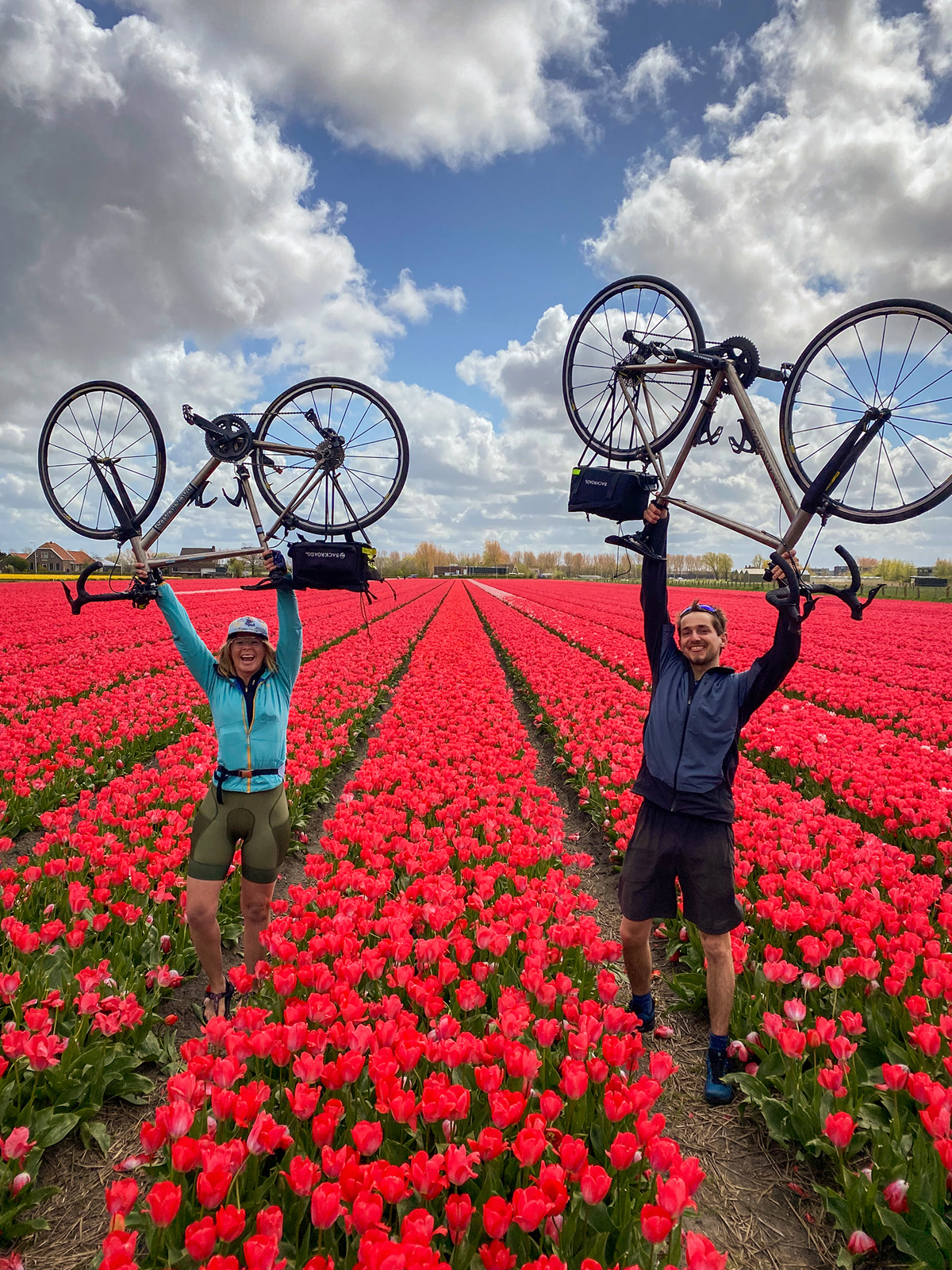 Man and woman carrying bikes in a field of red flowers