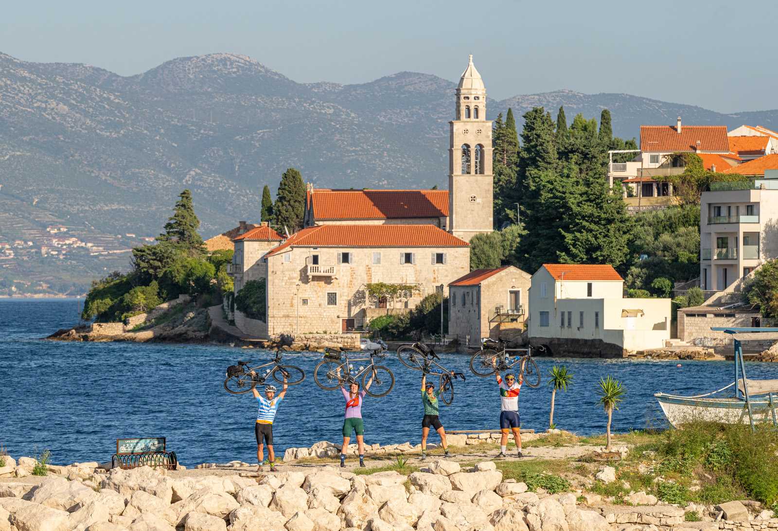 Group of people holding bikes over their heads, with a town and ocean in the background