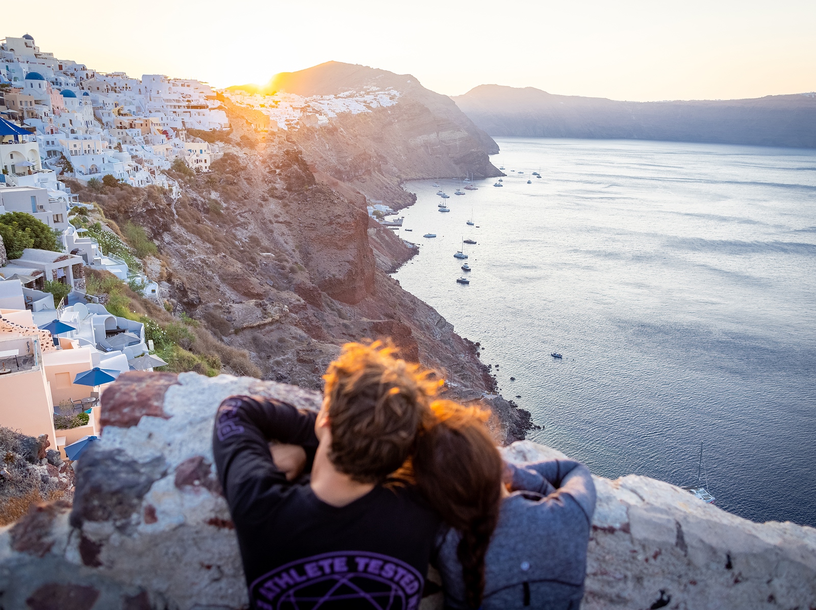 Man and woman leaning their heads on their shoulders, looking out to a large cliff full of houses
