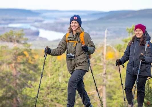 Two women with hiking poles ascending up a grassy hill