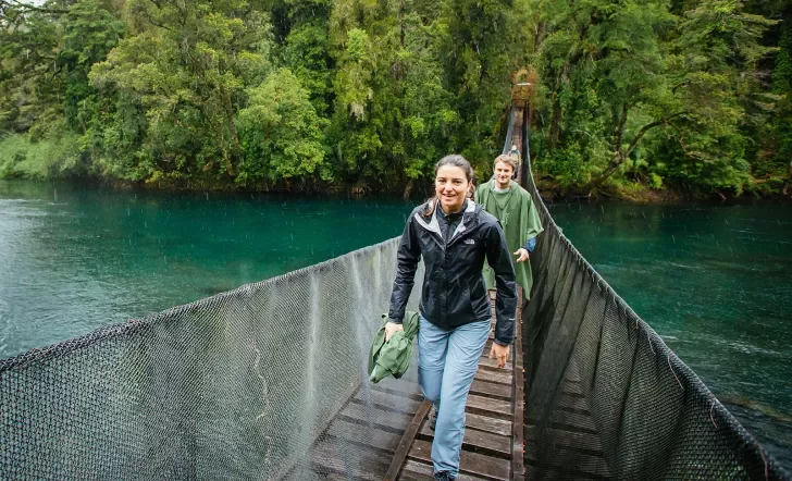 Group of guests walking over lake on rope bridge.