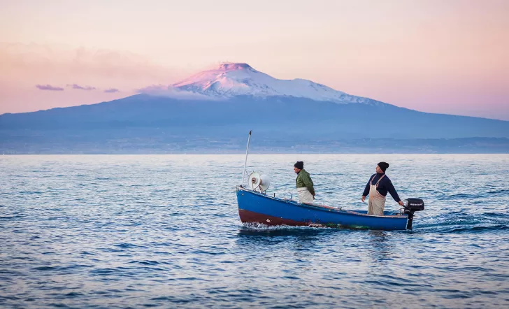 Two locals on boat during sunset, large mountain in distance.