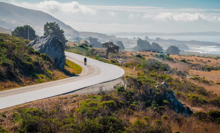 Coastal California vista, ocean and cliffs in background, cyclist in foreground.