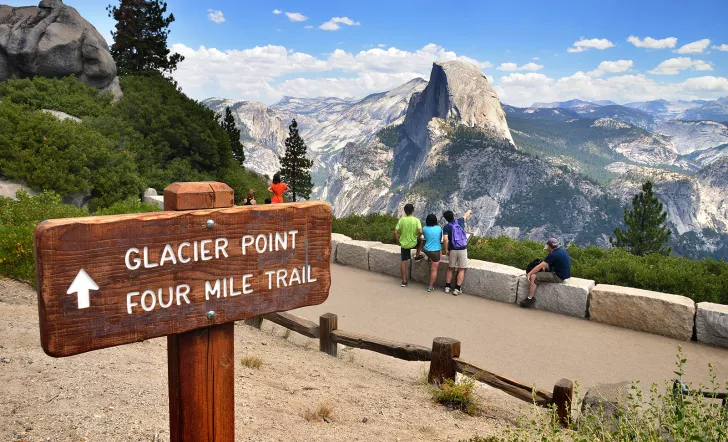 "GLACIER POINT" sign in foreground, guests and mountain in background.