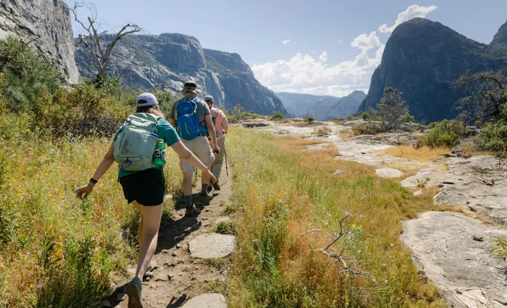 Three guests hiking through valley, mountains all around them.