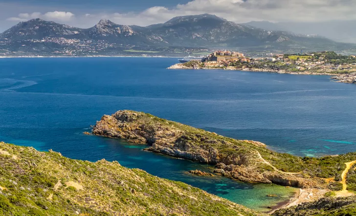 Wide shot of Italian lakeside, large peninsula, hills, coastal town in distance.