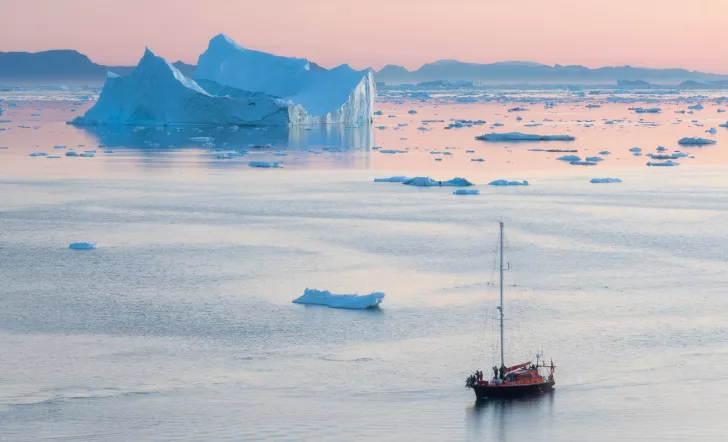 a ship floating on reflective water during a pink sunset