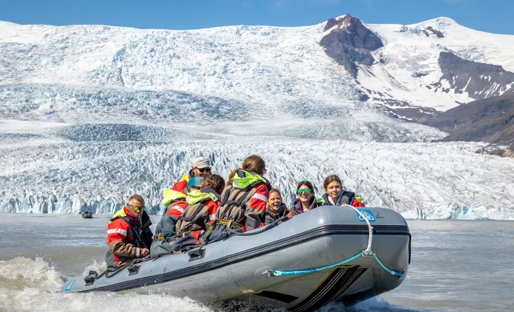 Group of people on a gray raft with snow mountains in the background