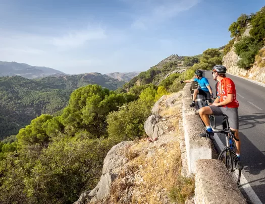 Bikers resting with bikes on side of a road in Spain, admiring a view.