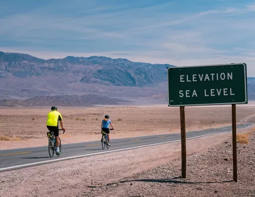 Cyclists on the road in California desert Elevation Sea Level sign