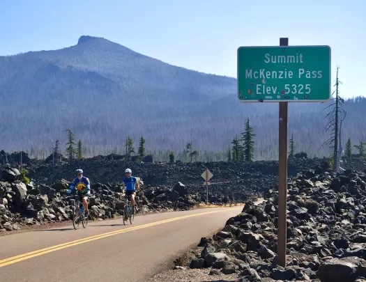 Two guests cycling past "MCKENZIE PASS" sign.