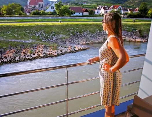 Person overlooking a ship balcony at rural countryside along the Danube River.