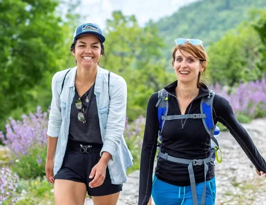Two hikers on a trail with wildflowers.
