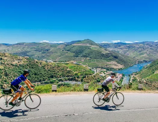 Two bikers riding on a road along the Douro River.