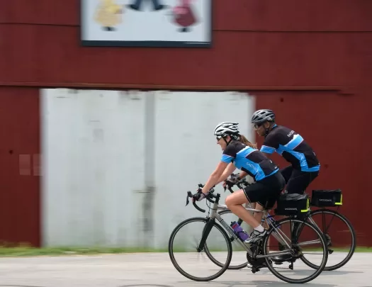 Two guests cycling past red barn.