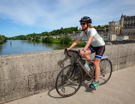 Guest cycling over concrete bridge, river, riverside town behind her.