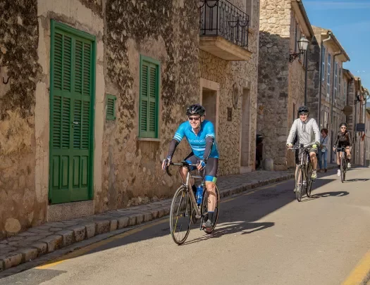 Bikers riding past stone facade houses in Spain.
