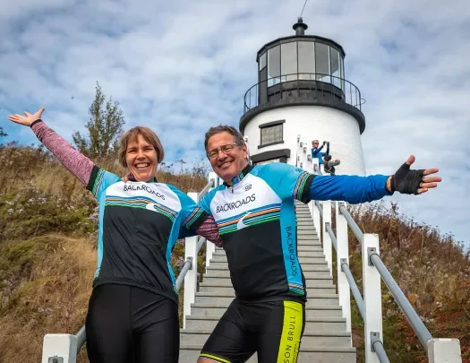 Two guests with their arms outstretched, lighthouse in background.