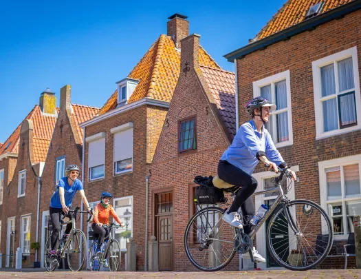 Three guests cycling past brick housefronts.