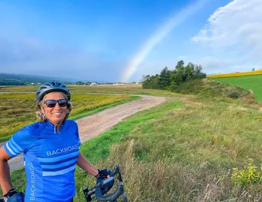Guest smiling on trail in foreground, rainbow in background.