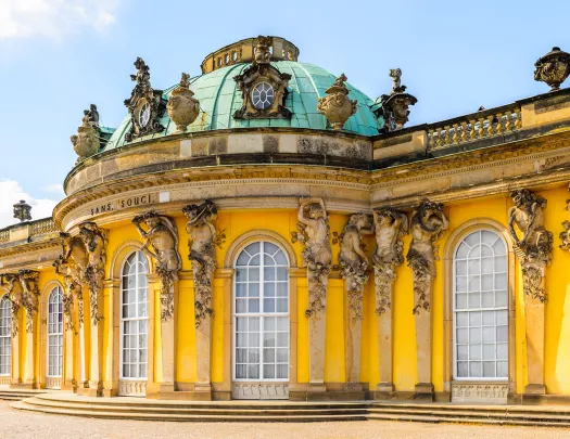 Sans Souci building in Germany, bright yellow decorated with statues of cherubs.