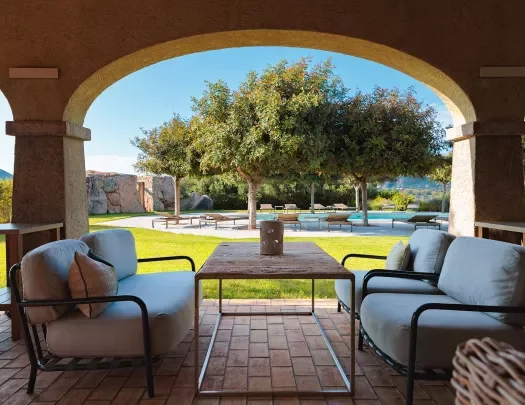 Shot of poolside at hotel, recliners, table, archway in foreground.