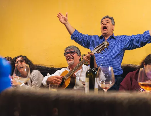 Guests at meal, one playing guitar, other singing behind them.