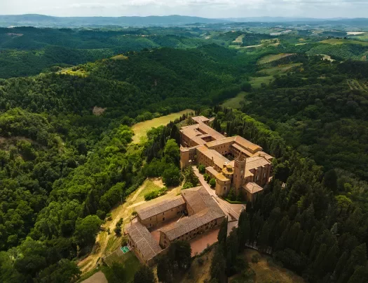 Bird's eye shot of Italian countryside, forests, castle, hills visible.