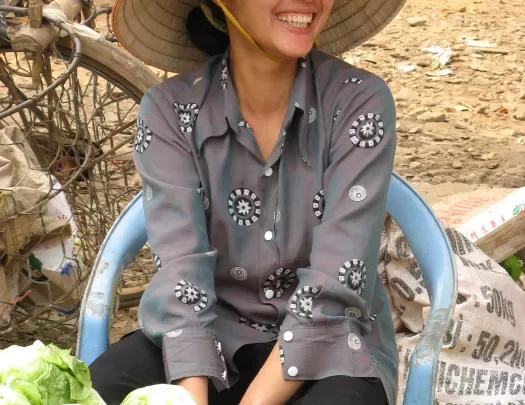 Local smiling in front of vegetable stand.