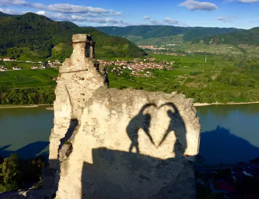 Shadows of two people making a heart with their arms.