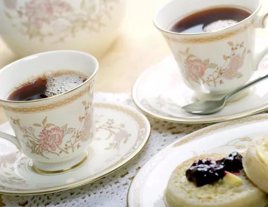 Ornate English cups of tea and english muffins with butter and jam.