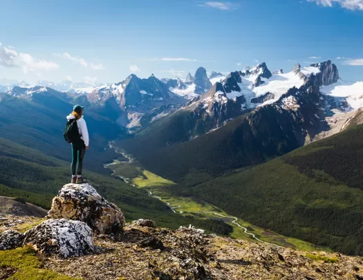 Guest standing on rocky hilltop, looking towards larger mountains.
