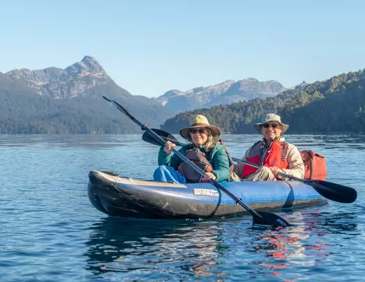 Two guests kayaking, sharp mountains in distance.
