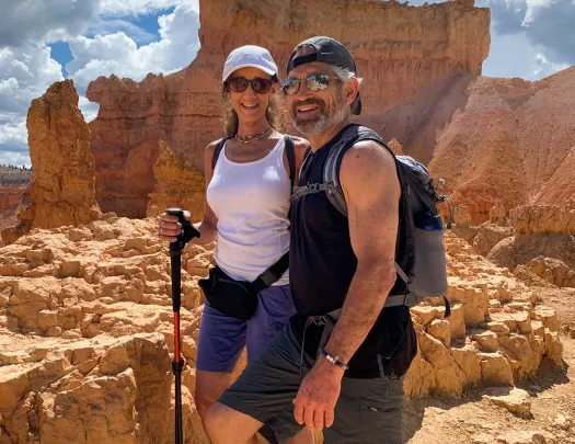 Two guests in hiking gear, posing for camera in front of desert plateau.