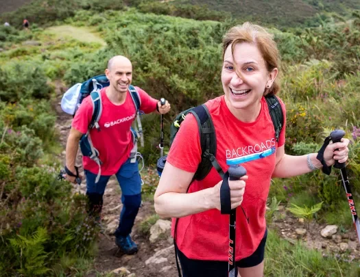 Two guests with poles walking up trail, smiling at camera.