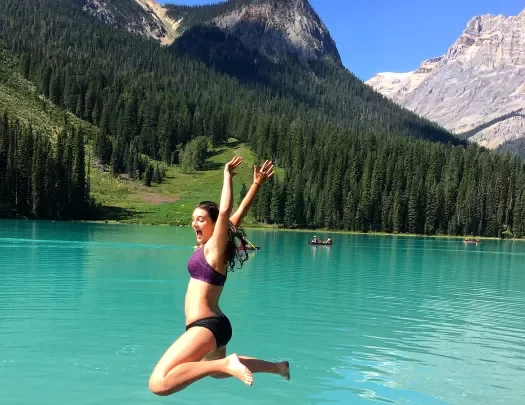 Guest jumping into light blue lake, mountain in background.