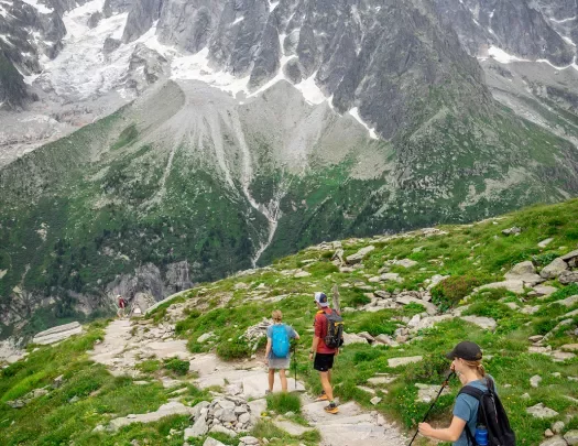 Three guests walking down mountainside, large, spiky peaks in distance. 