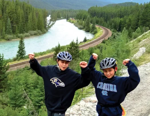Two young guests with their hands above their heads, river, forest, road behind them.