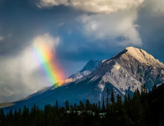 Shot of mountain range, clouds, rainbow visible.