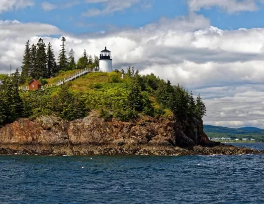 Wide shot of small island, white lighthouse and small red building on it.
