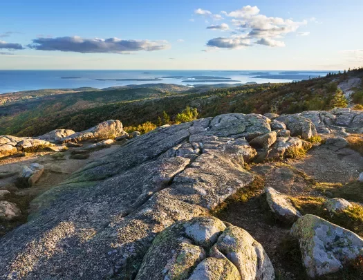 Wide shot of rocky coastline, ocean and small islands visible in background.