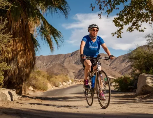 Guest cycling past palm tree, desert landscape behind him.