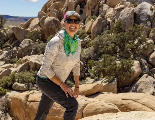 Guest hiking up desert boulder, craggy sandstone rocks in background.