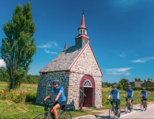 Four guests cycling past small brick building.