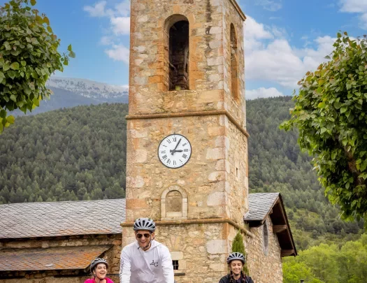Three people biking past an old stone church