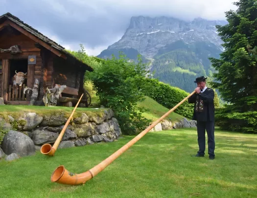 Local man playing a Swiss Horn, wooden shack in background.