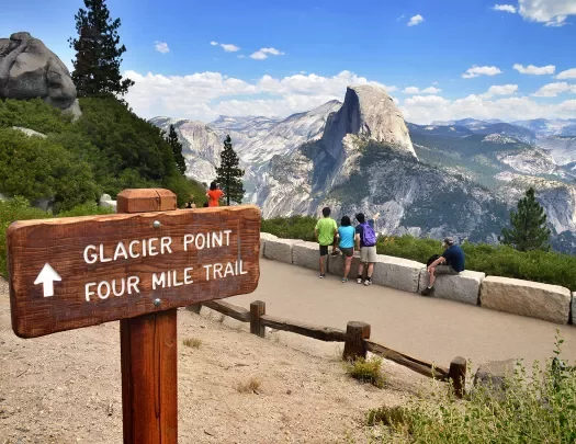 "GLACIER POINT" sign in foreground, guests and mountain in background.