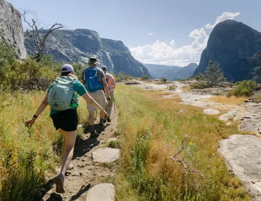 Three guests hiking through valley, mountains all around them.