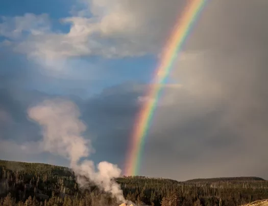 Geyser expelling steam and connecting with the end of a rainbow