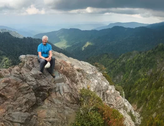 Guest sitting on rocky cliff-top. Overlooking forested valley.